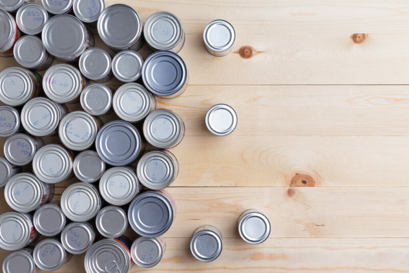 Conceptual background of multiple canned foods in sealed aluminum tins or cans of varying sizes arranged on a wooden table with copy space, overhead view