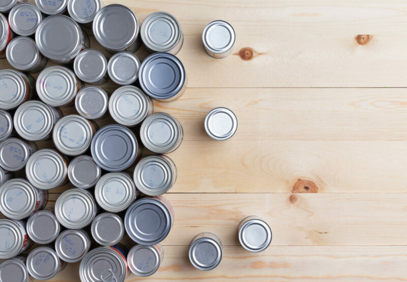 Conceptual background of multiple canned foods in sealed aluminum tins or cans of varying sizes arranged on a wooden table with copy space, overhead view